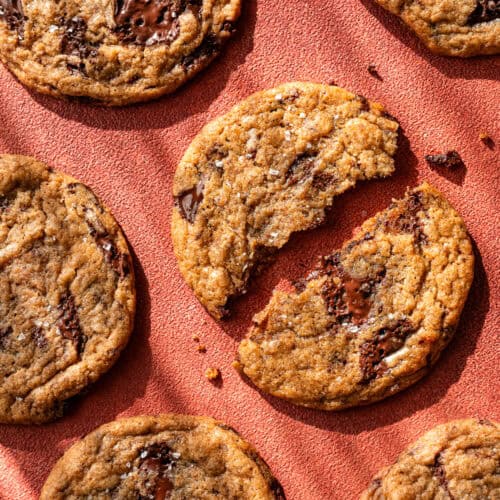 baked chocolate chip cookies on a red table, one torn in half.