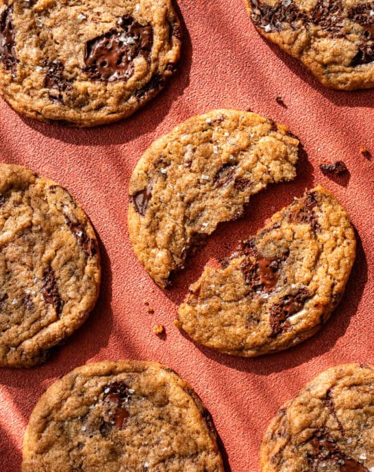 baked chocolate chip cookies on a red table, one torn in half.