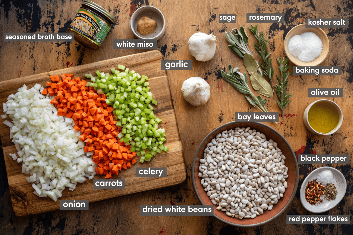 ingredients for white bean soup on a wooden table with ingredients labeled. 