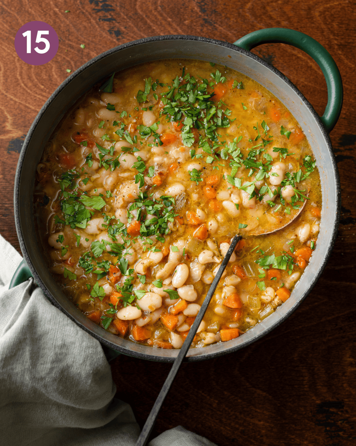 green dutch oven filled with white bean soup with carrots, ladle dug in.