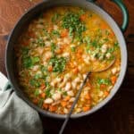 green dutch oven filled with white bean soup with carrots, ladle dug in.