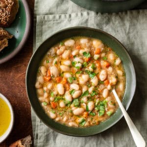 brothy white bean soup in a green bowl on a linen towel on a wooden table.