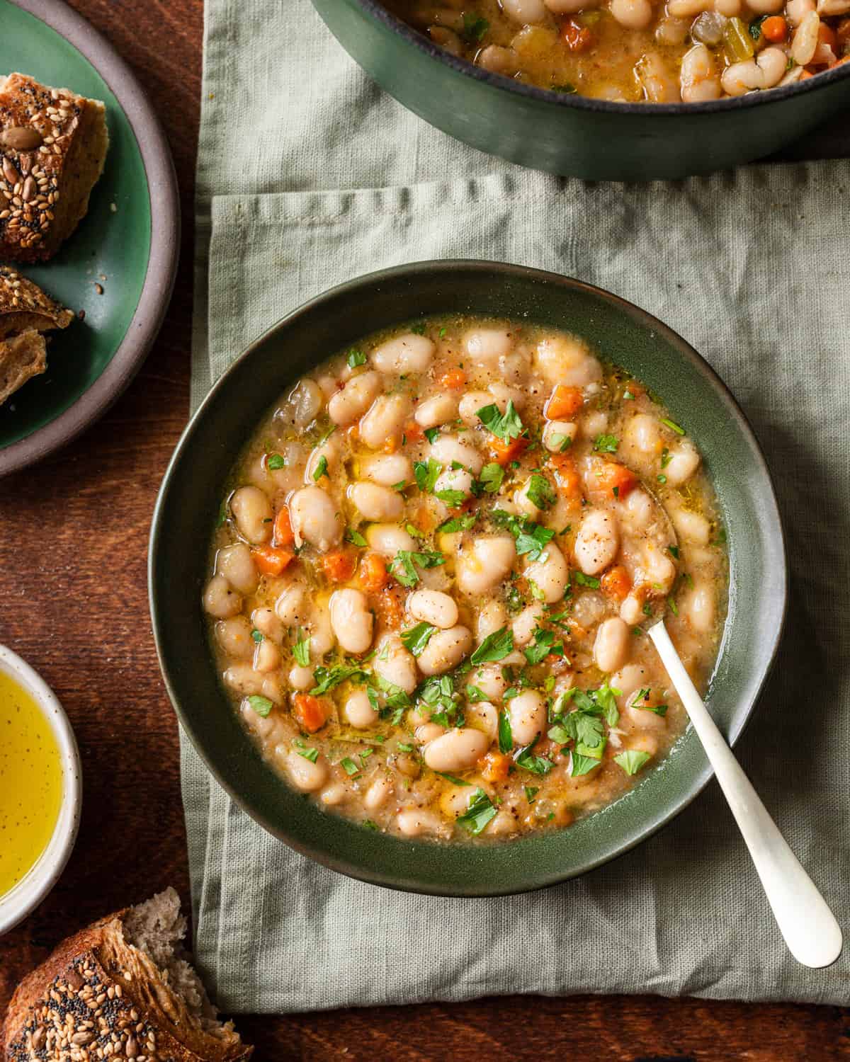 brothy white bean soup in a green bowl on a linen towel on a wooden table.