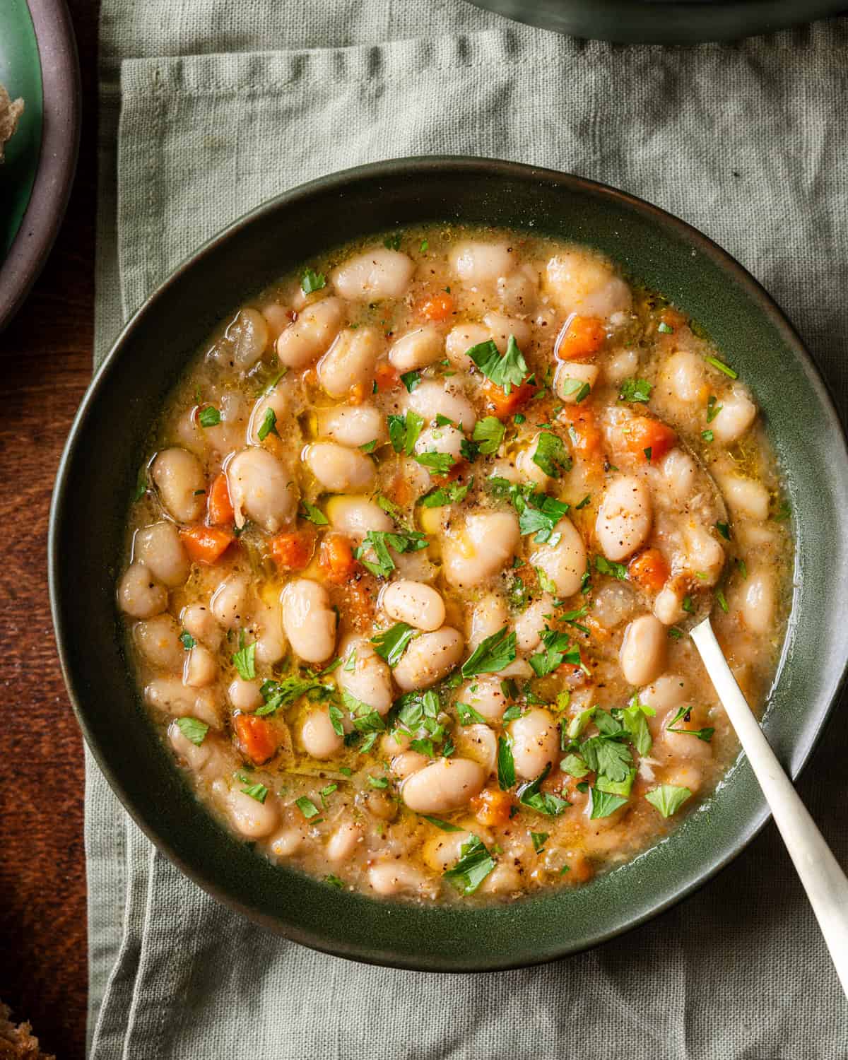 brothy white bean soup in a green bowl on a linen towel.