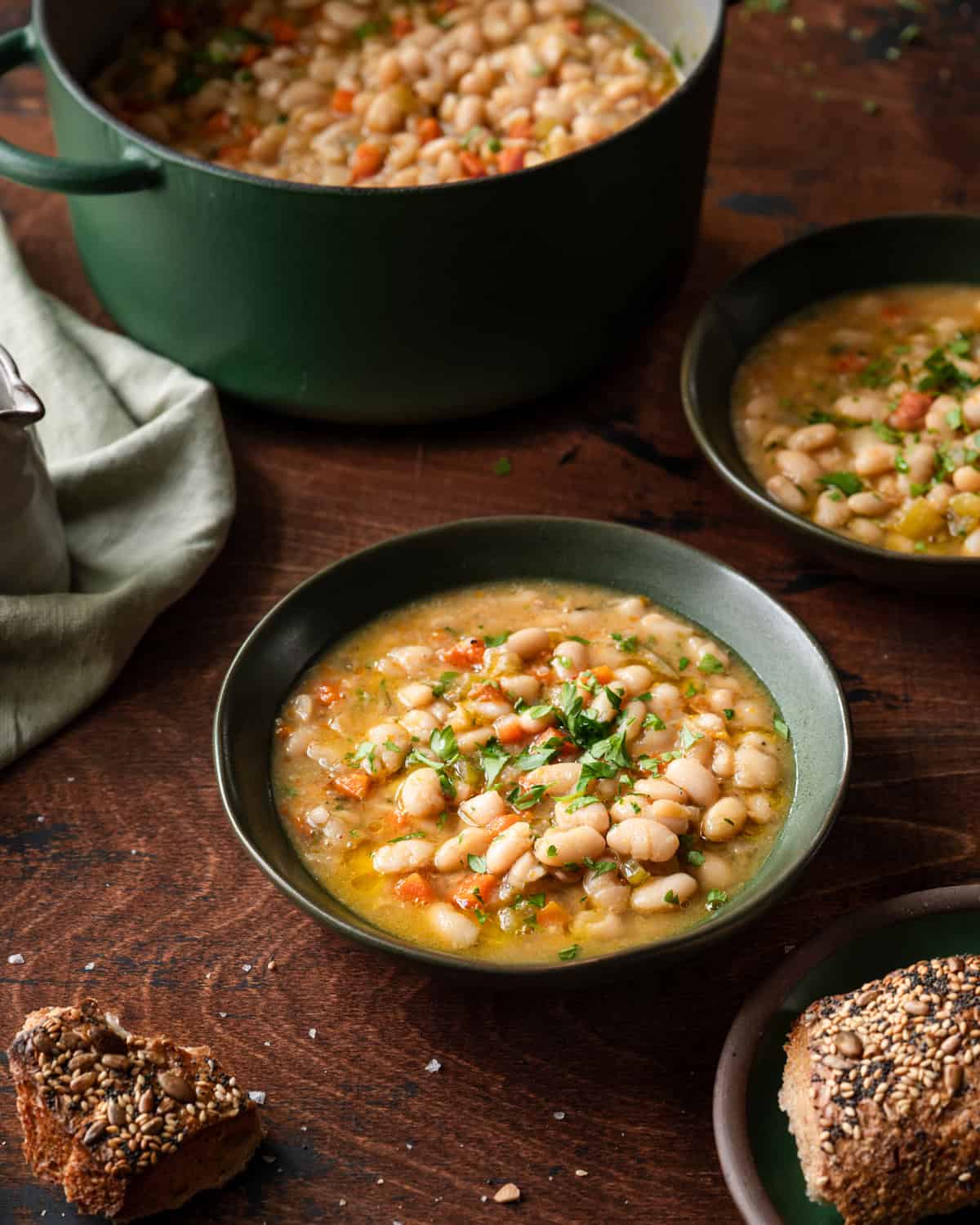 white bean soup in two green bowls on a wooden table with dutch oven in the back.