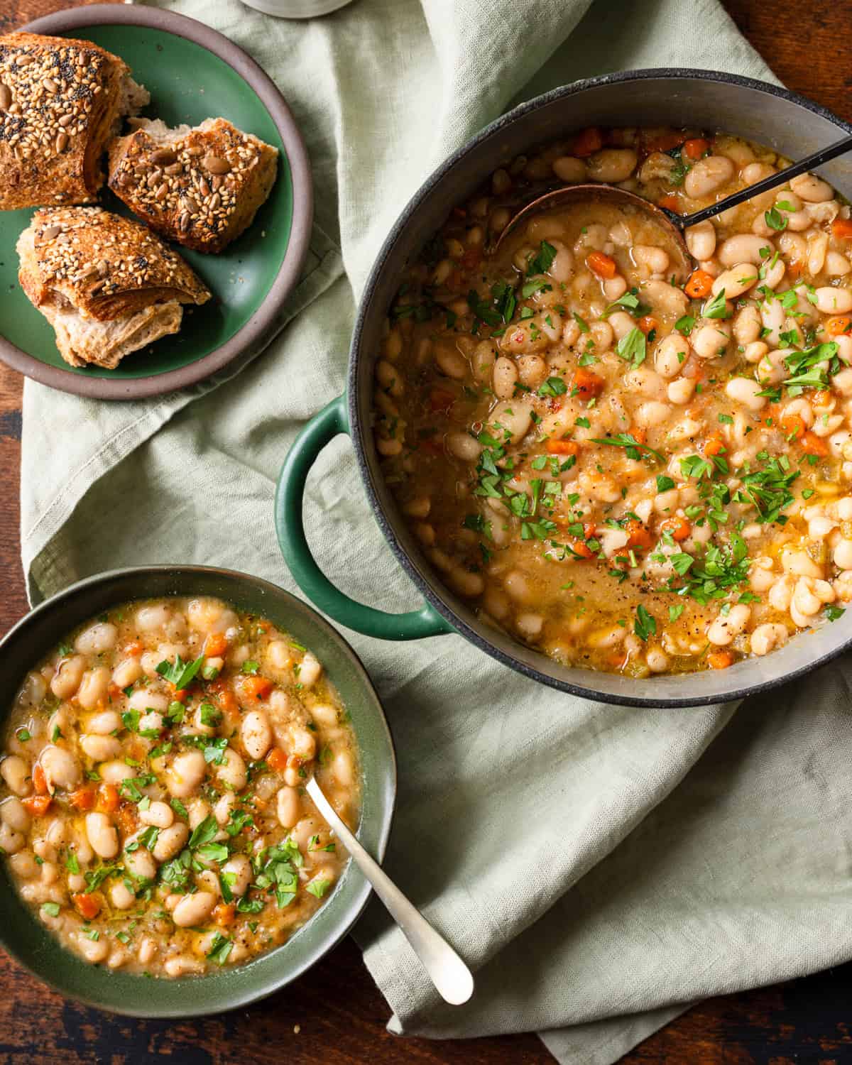 a green dutch oven and green bowl with white bean soup on a linen towel.