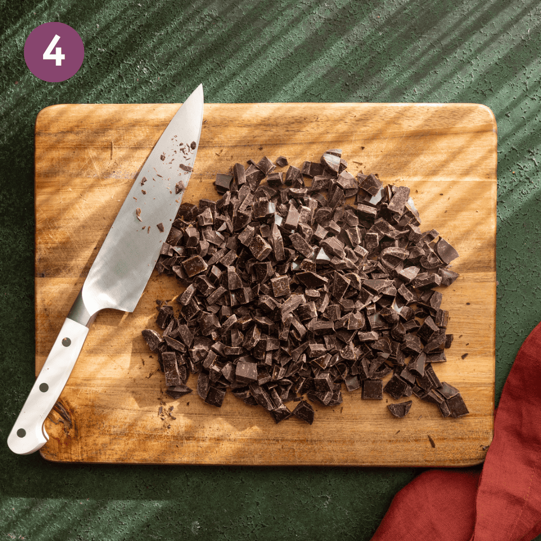 chopped dark chocolate with a knife on a wooden cutting board.