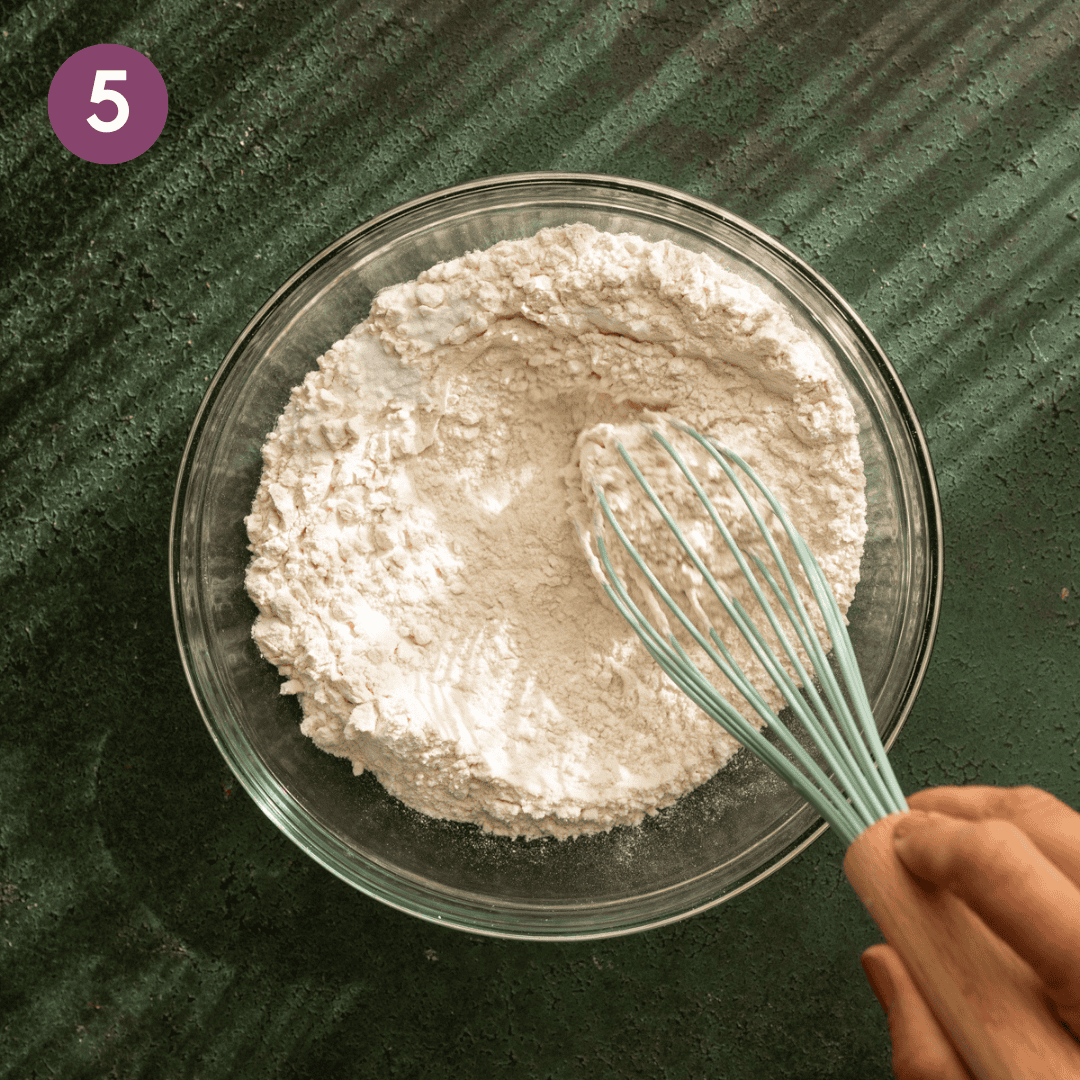 person whisking dry ingredients in a glass bowl.