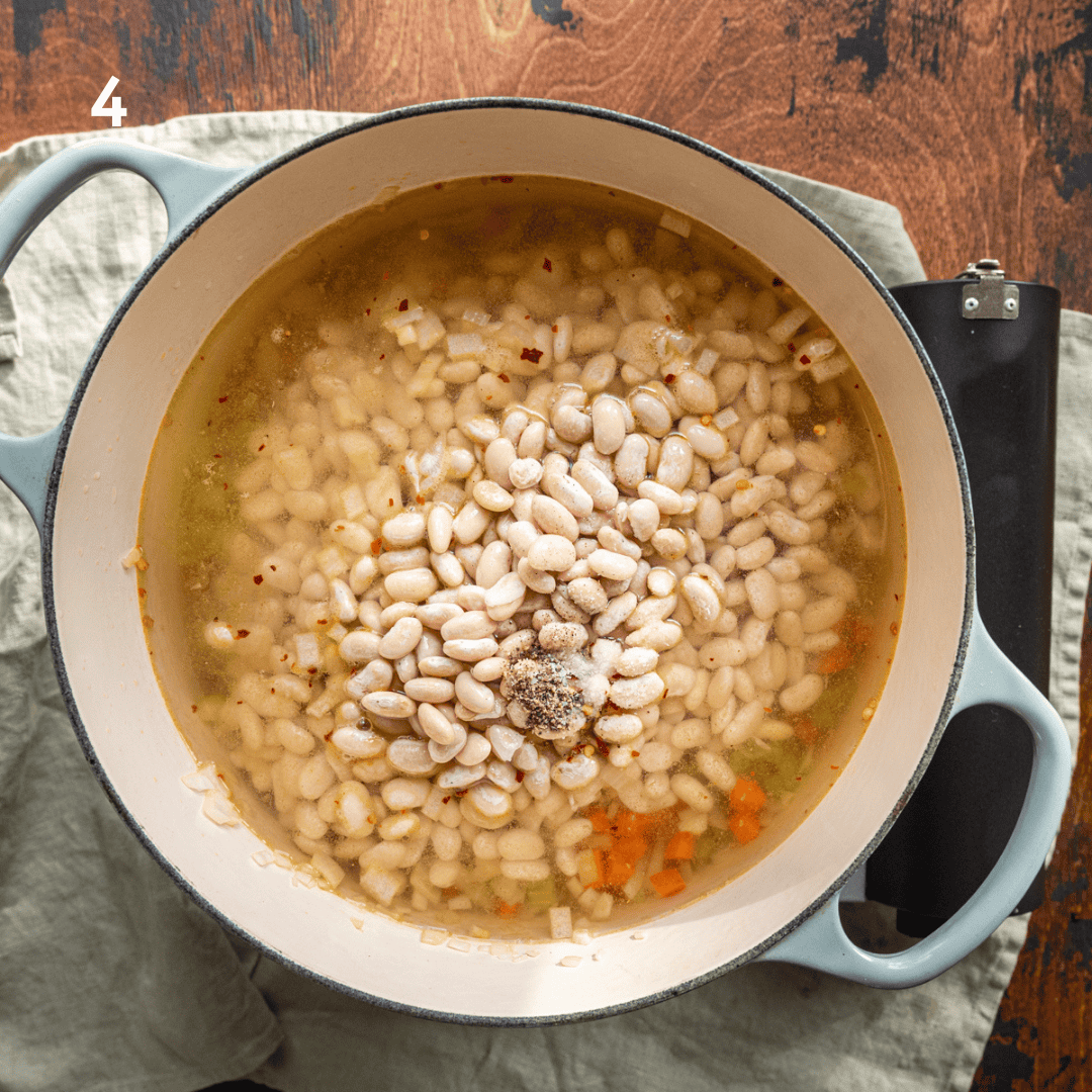 dried white beans and water in a dutch oven with carrots, celery, and onions.