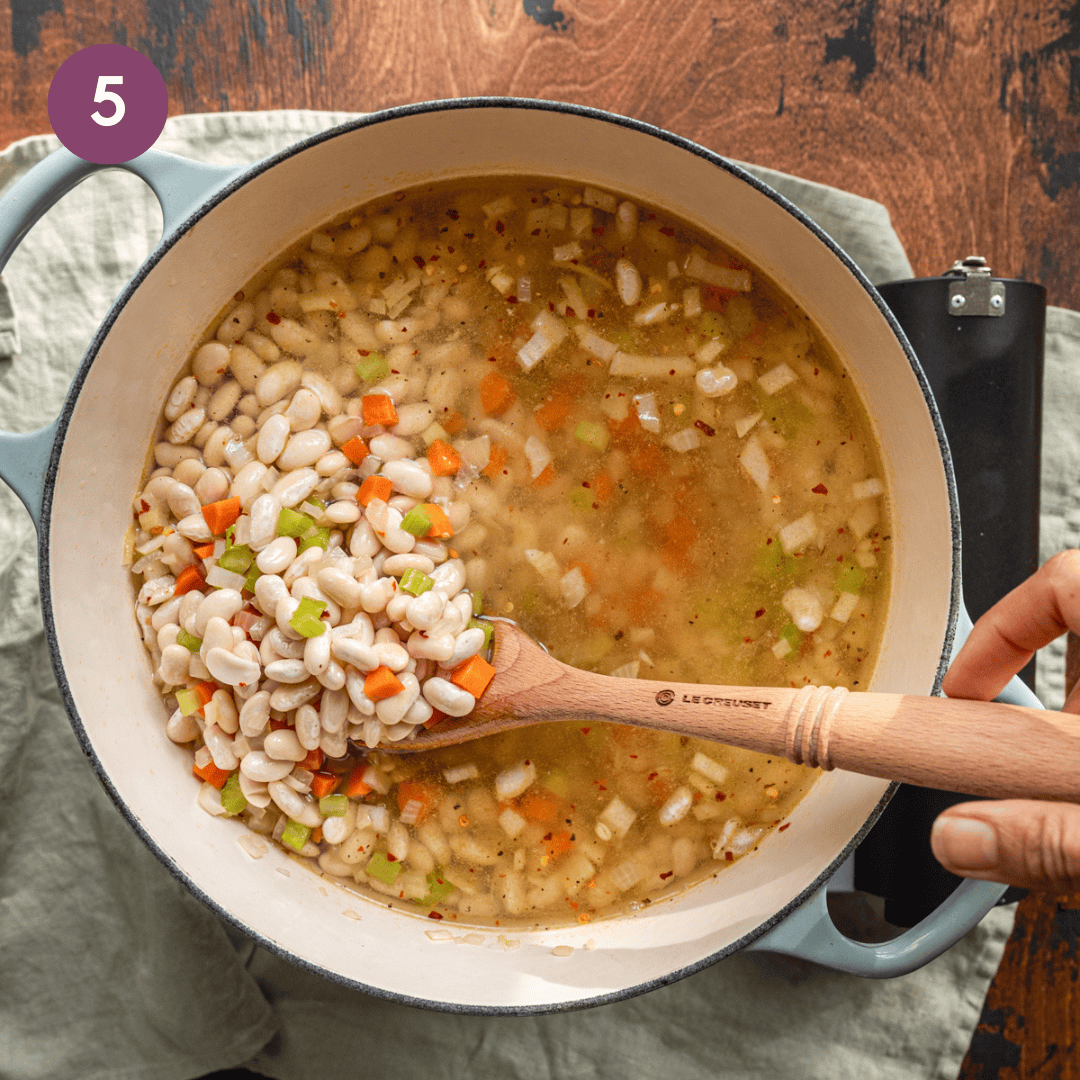 wooden spatula stirring dried white beans in broth for a soup.