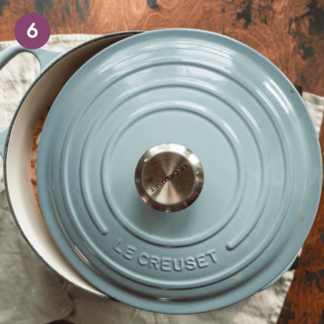 light blue dutch oven on a wooden table with lid partially covered.