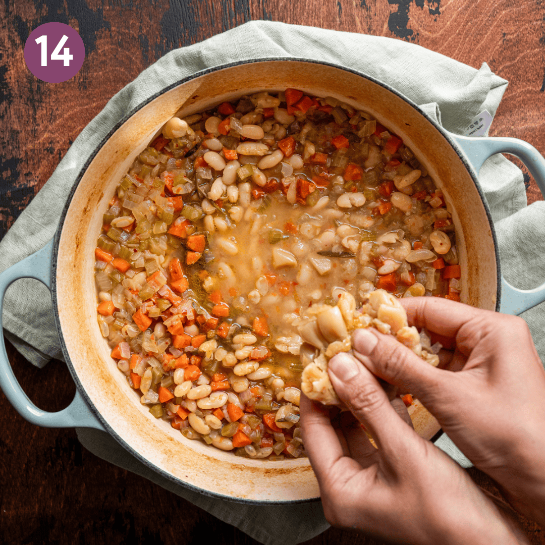 woman's hands squeezing roasted garlic cloves into a pot of white bean soup. 