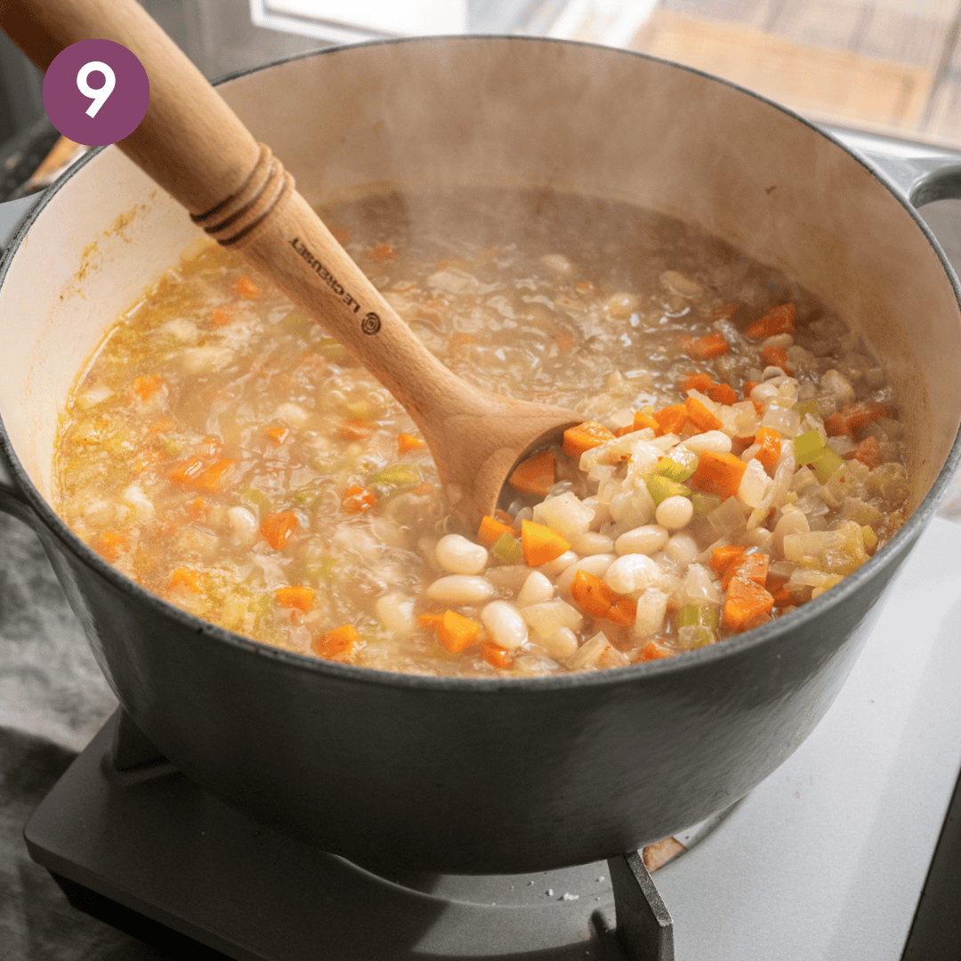 wooden spatula stirring a white bean soup with carrots, before beans are cooked.