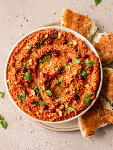 overhead shot of muhammara in a large shallow bowl surrounded by pieces of pita.