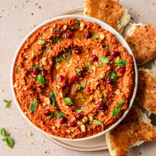 overhead shot of muhammara in a large shallow bowl surrounded by pieces of pita.