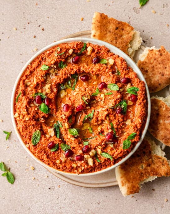 overhead shot of muhammara in a large shallow bowl surrounded by pieces of pita.