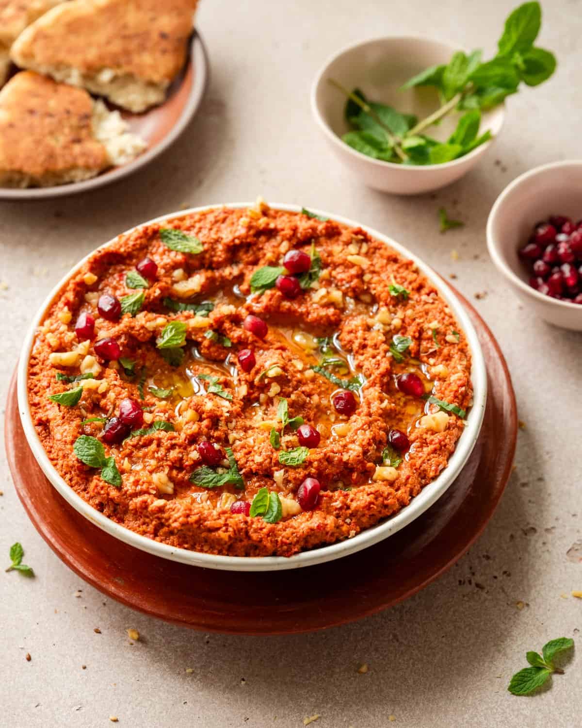 45 degree angle perspective of muhammara next to ingredient bowls and pita bread.