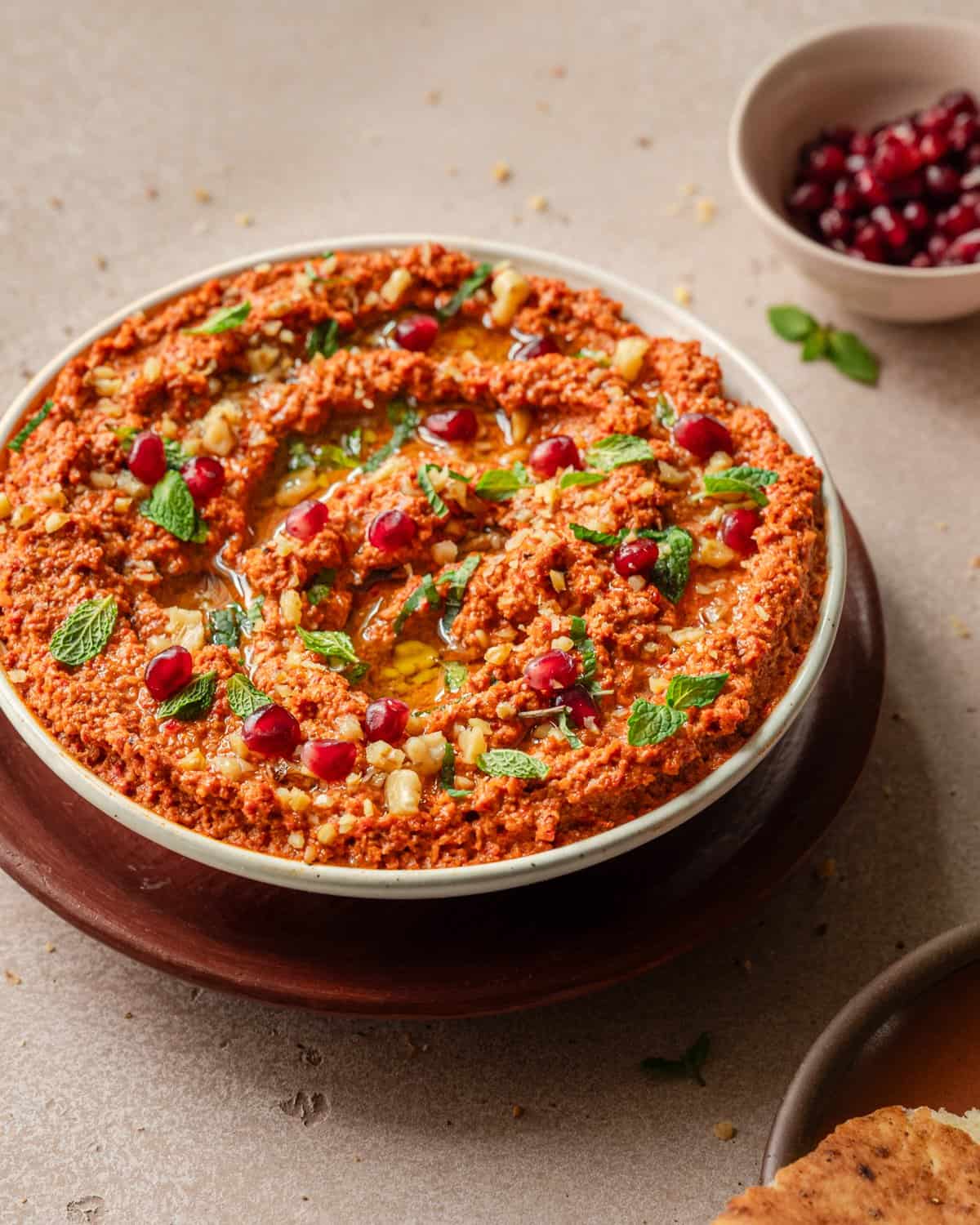 close up side view of bowl of muhammara with herbs, pomegranate seeds and walnuts.