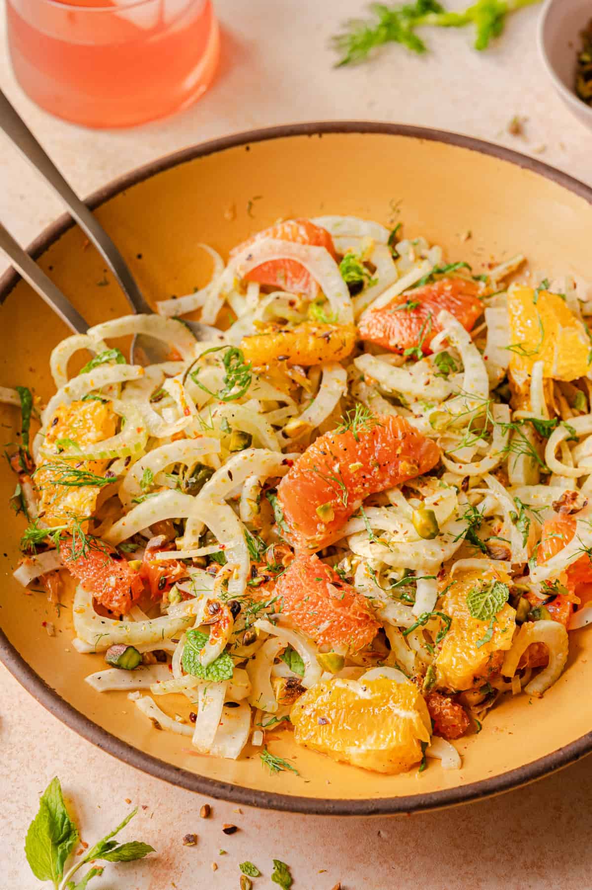 closeup shot of a fennel orange salad in a yellow bowl on a pink surface.