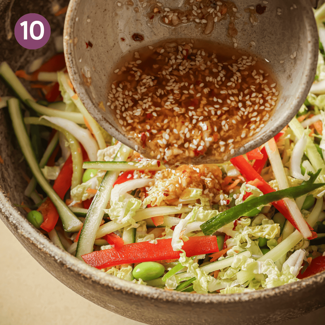 person pouring sesame sauce over mixed veggies.