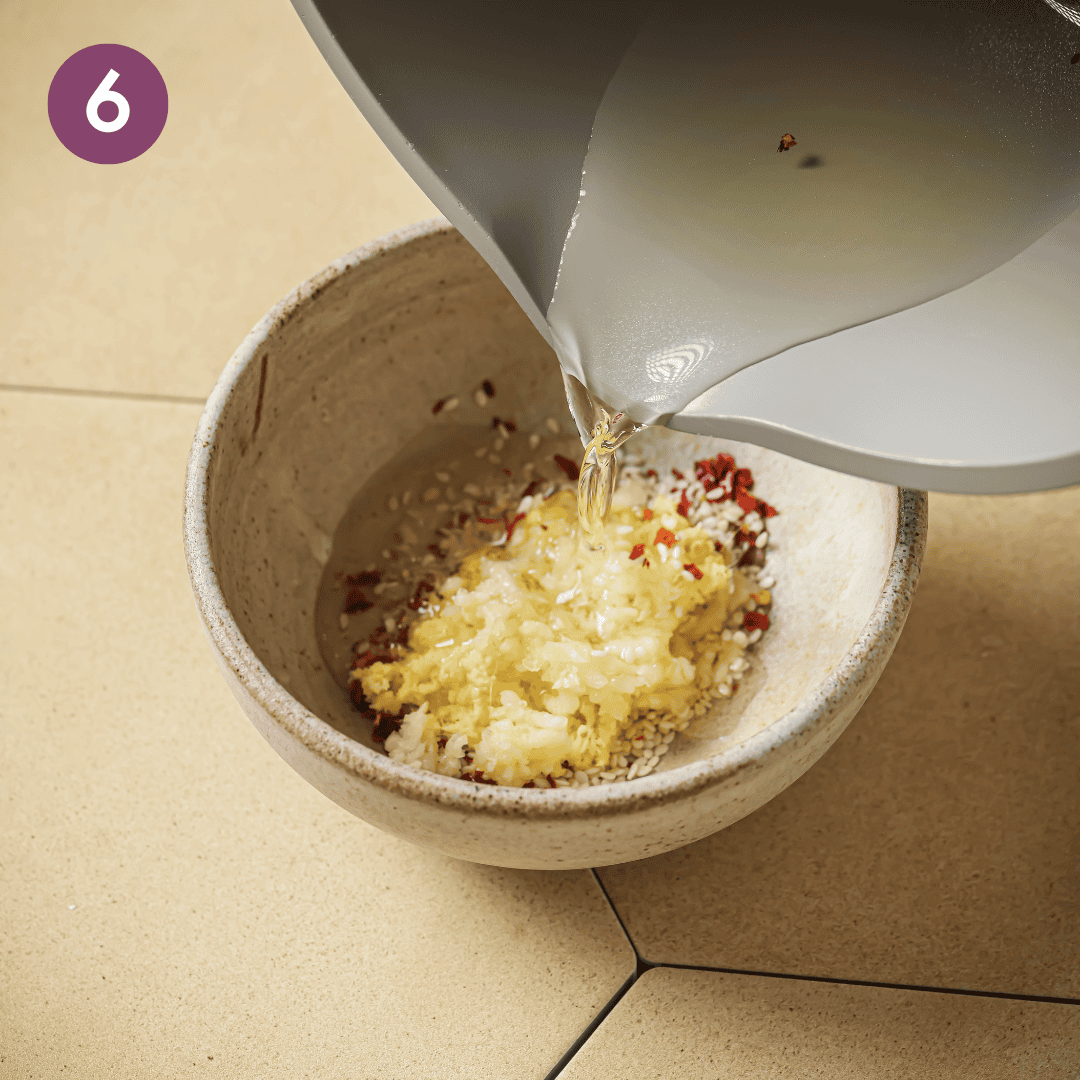 person pouring hot oil over ingredients in the bowl.