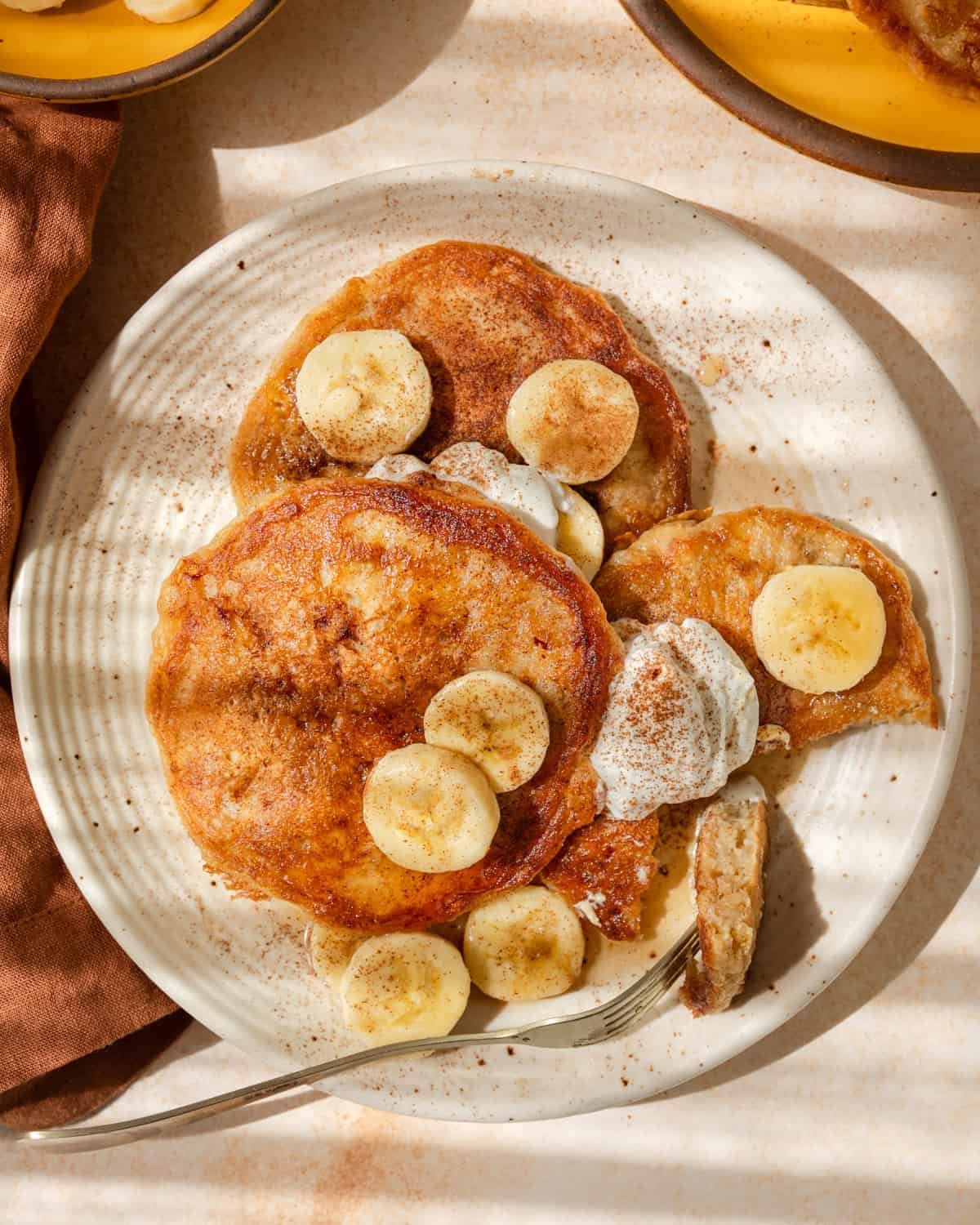 Overhead photo of person taking a bite from 3 banana pancakes on a plate.