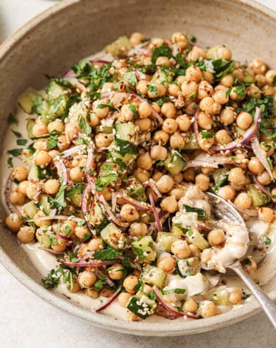 Angled overhead shot of chickpea salad in a beige bowl with a spoon.