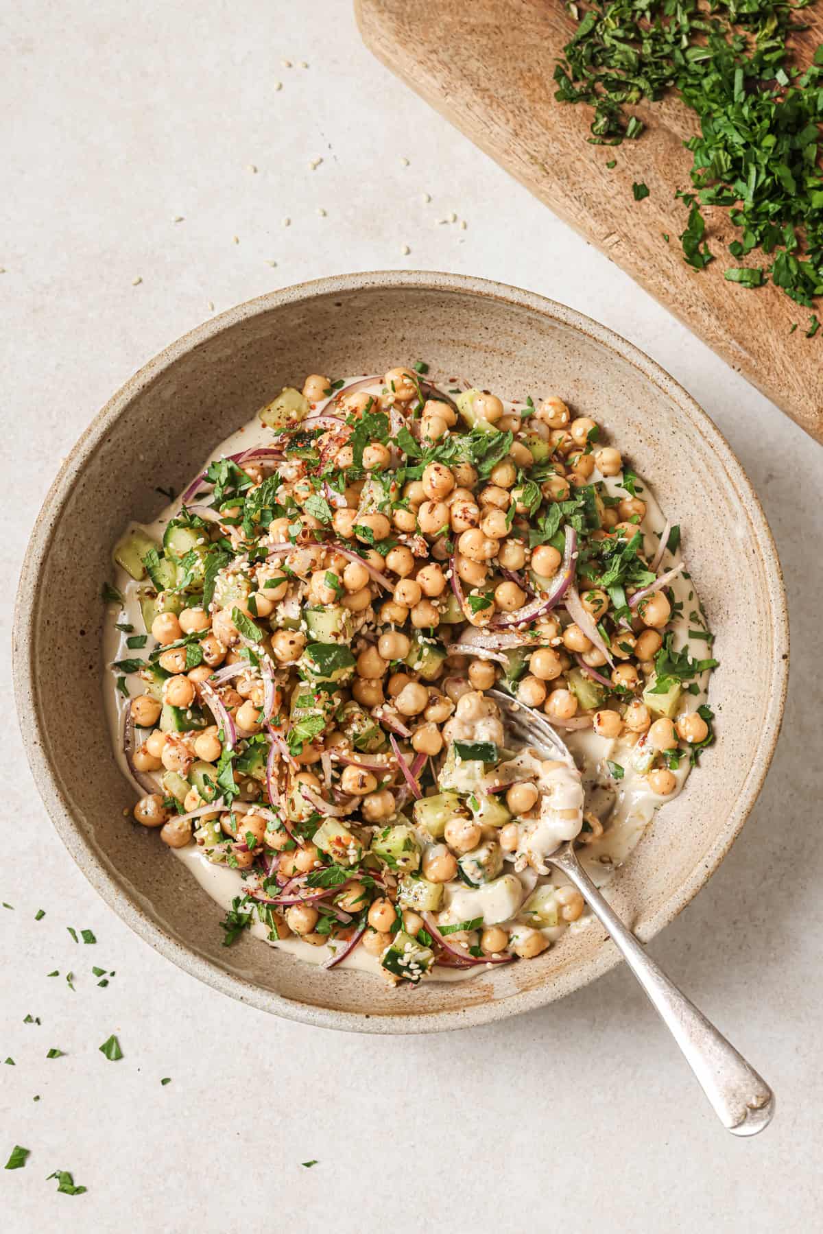 Overhead shot of chickpea salad next to a cutting board with chopped herbs.