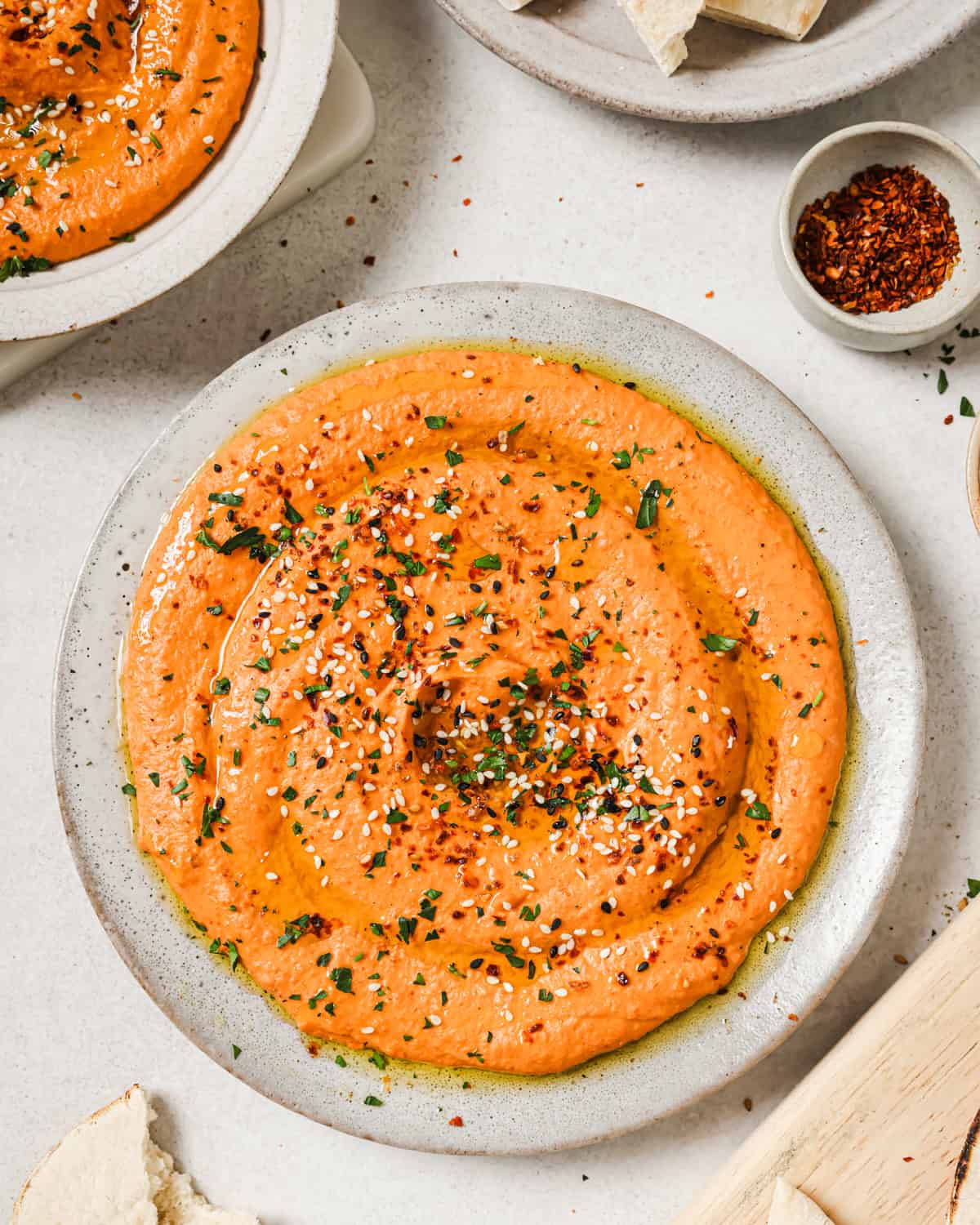 roasted red pepper hummus on a plate garnished with parsley, aleppo pepper and sesame seeds.