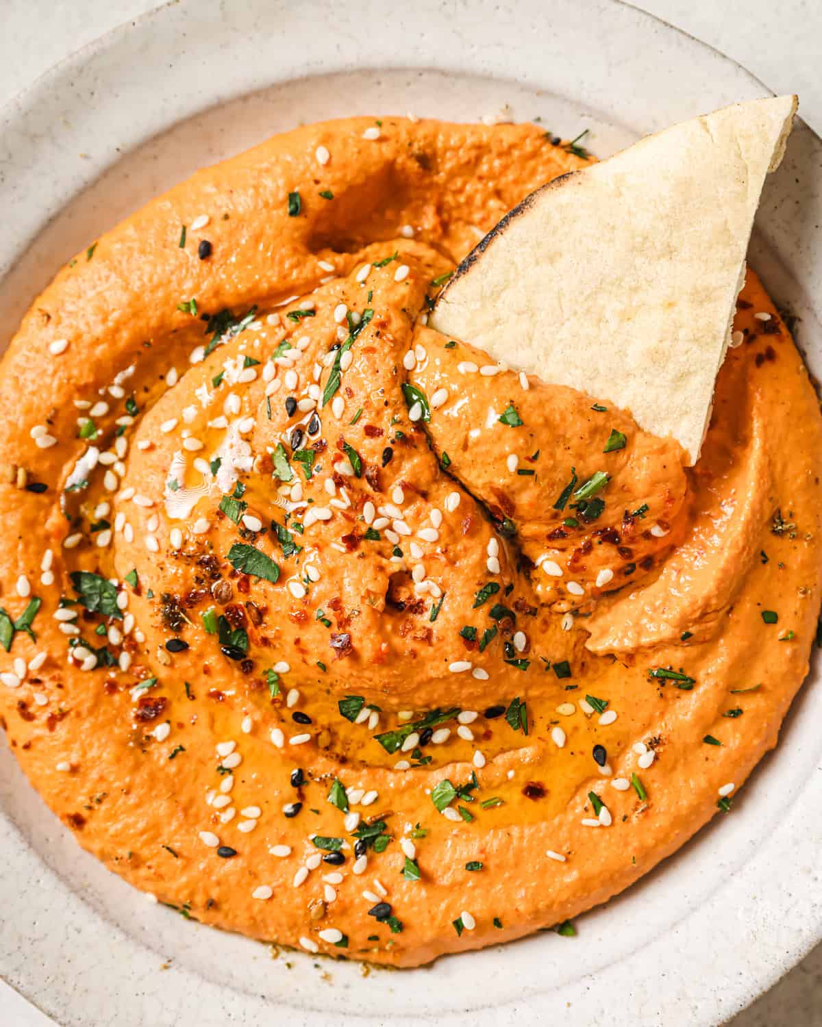 piece of pita bread in a bowl of red pepper hummus.