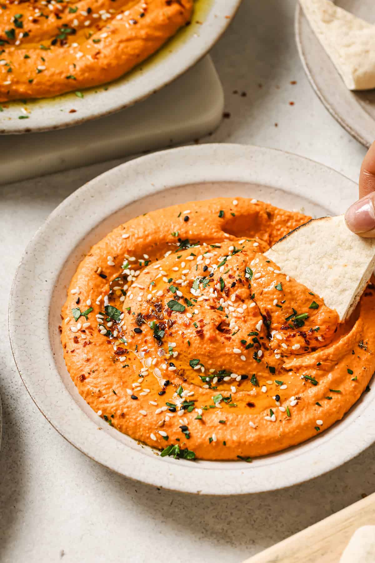 person dipping piece of pita bread into bowl of hummus.