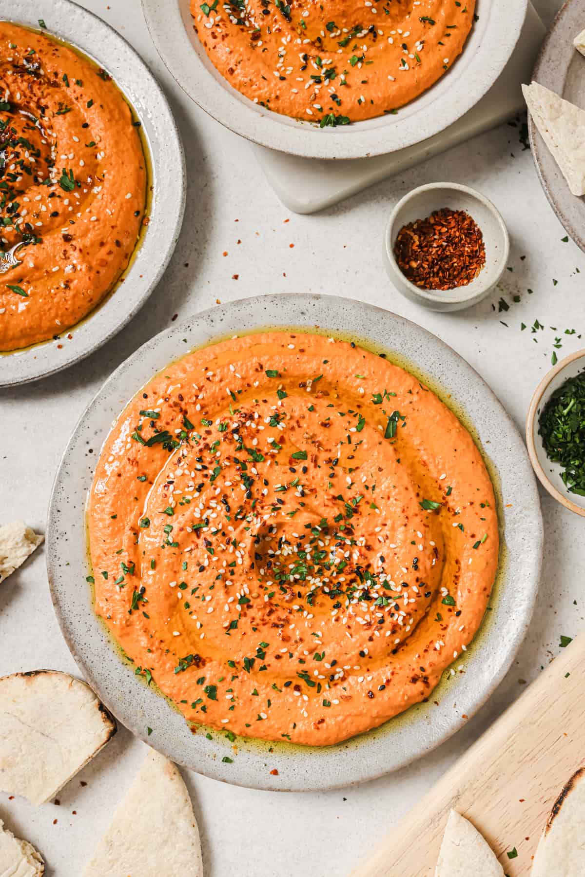three plates of roasted red pepper hummus on a table.