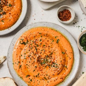 three plates of roasted red pepper hummus on a table.