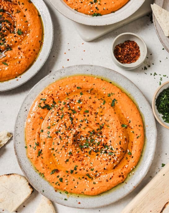 three plates of roasted red pepper hummus on a table.