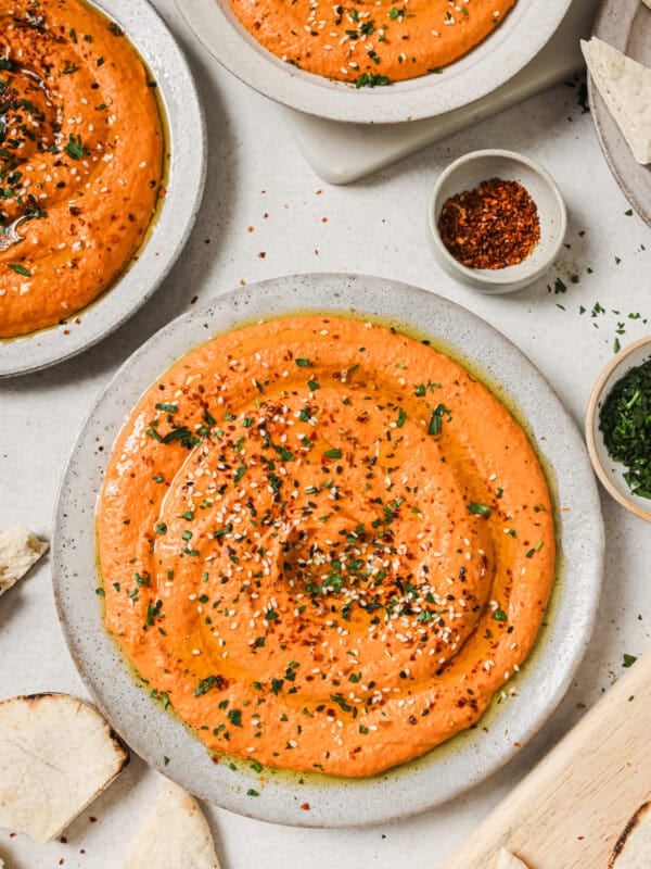 three plates of roasted red pepper hummus on a table.