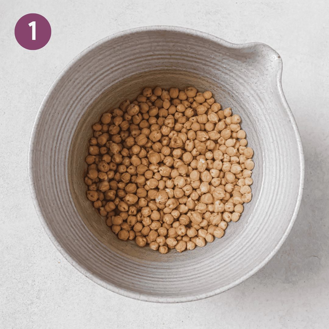 dried chickpeas soaking in a bowl covered in water.