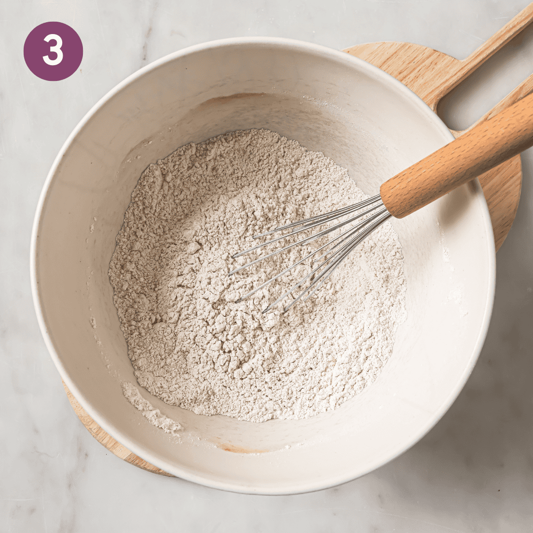 Person whisking dry ingredients in bowl.