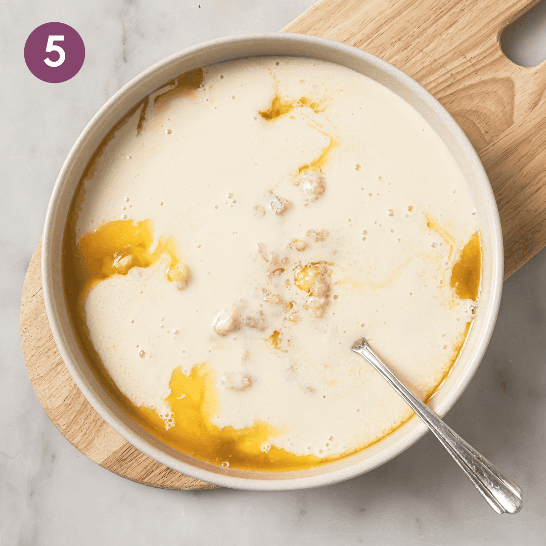 Liquid ingredients added to the mashed bananas in a bowl.