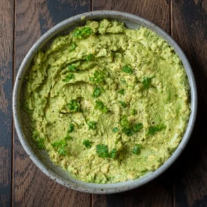 A bowl of guacamole with cilantro on a wooden table.