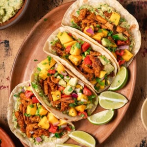 Flatlay of four vegan tacos with soy curls and mango salsa on wooden table.