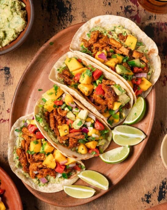 Flatlay of four vegan tacos with soy curls and mango salsa on wooden table.