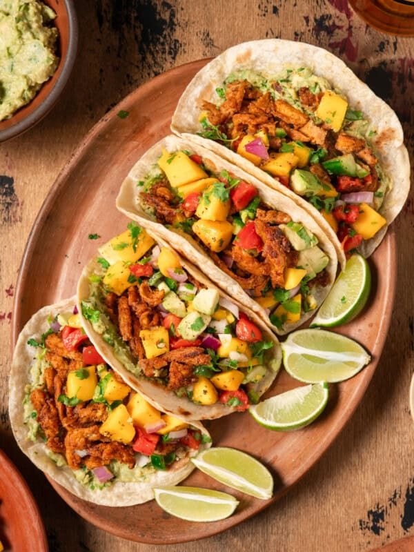 Flatlay of four vegan tacos with soy curls and mango salsa on wooden table.