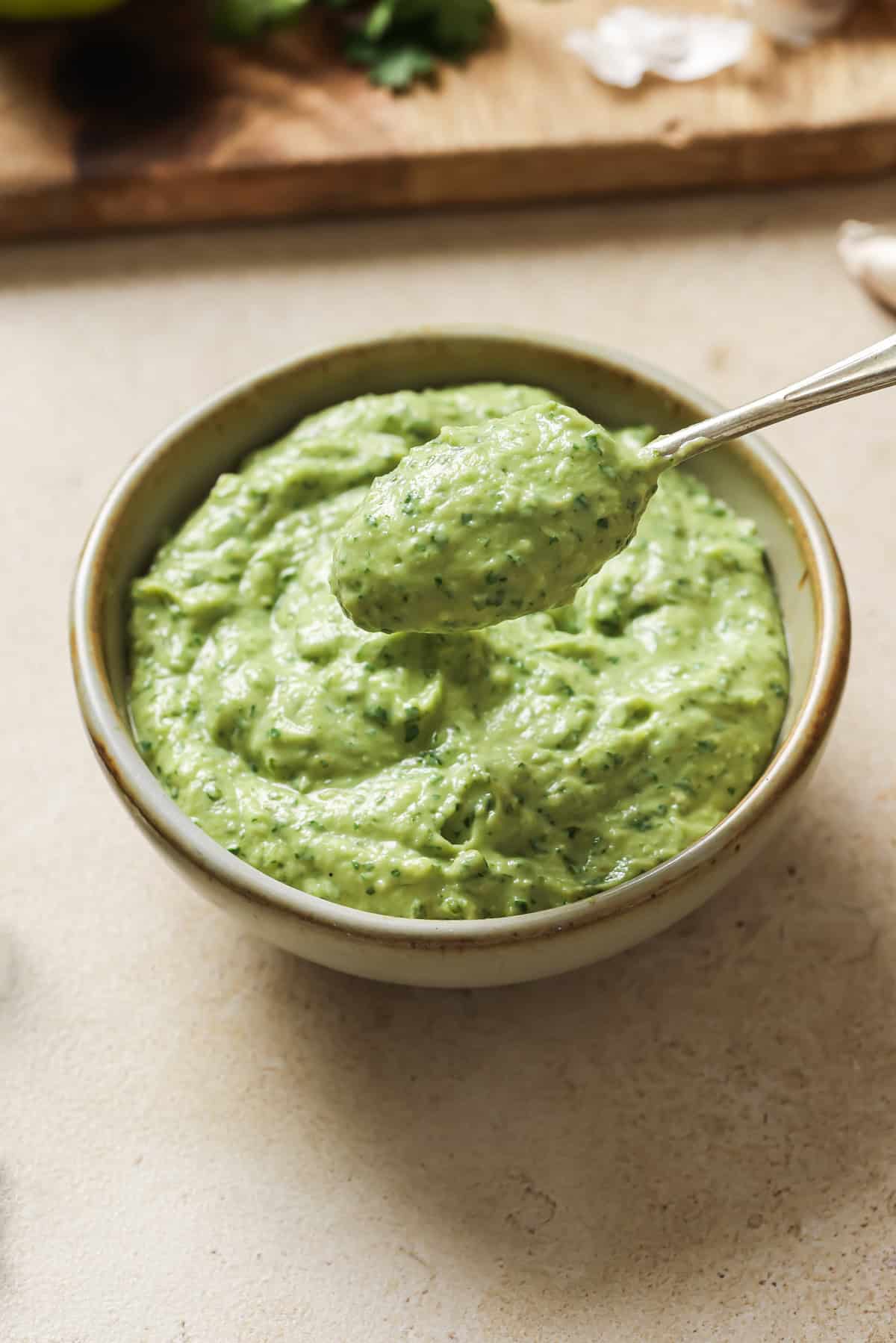 Person taking a spoonful of avocado crema from a small bowl.