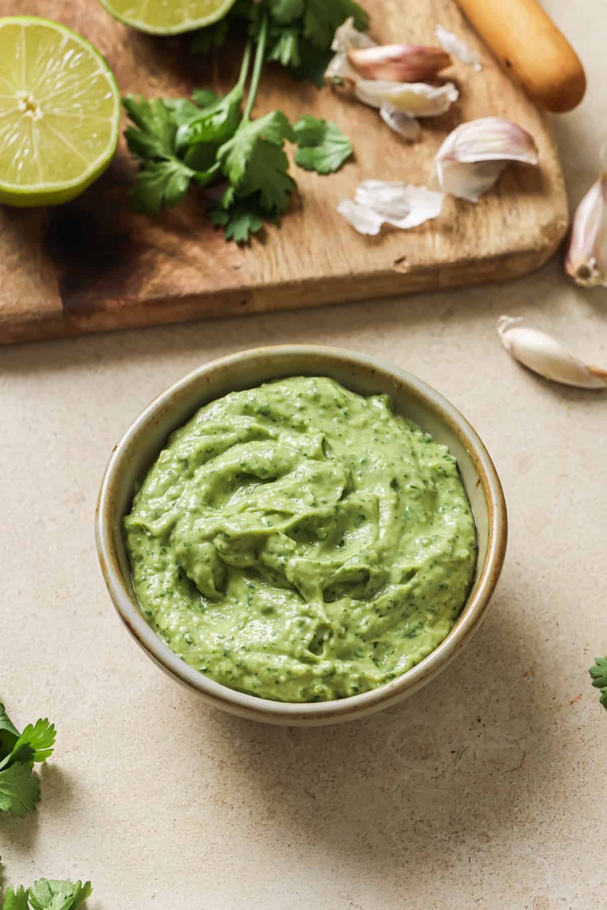 bowl of avocado crema next to wooden cutting board with ingredients on it.