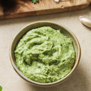 bowl of avocado crema on a table next to a cutting board with ingredients.