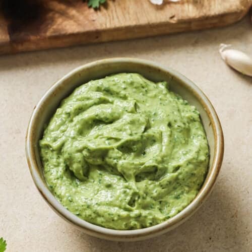 bowl of avocado crema on a table next to a cutting board with ingredients.