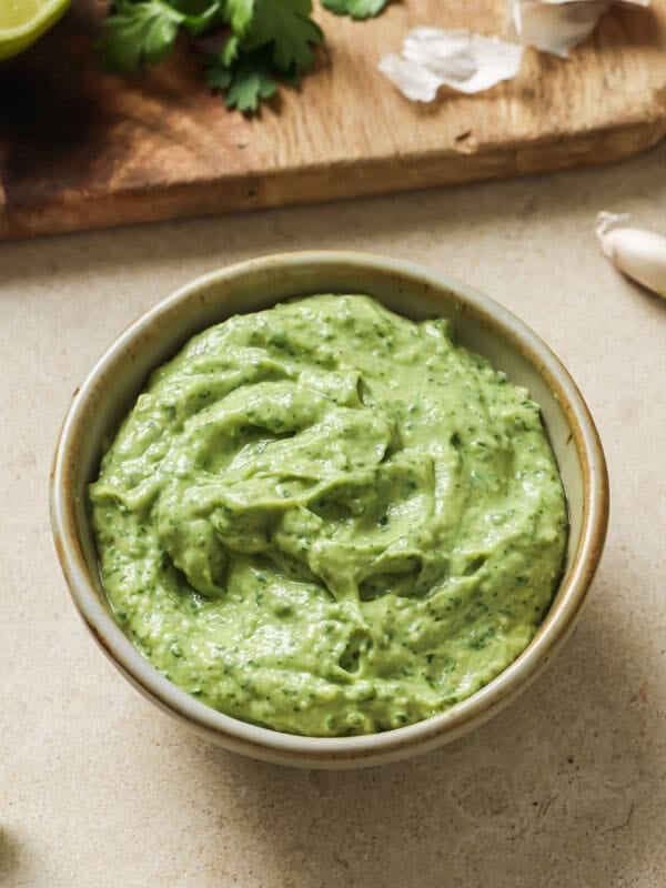 bowl of avocado crema on a table next to a cutting board with ingredients.