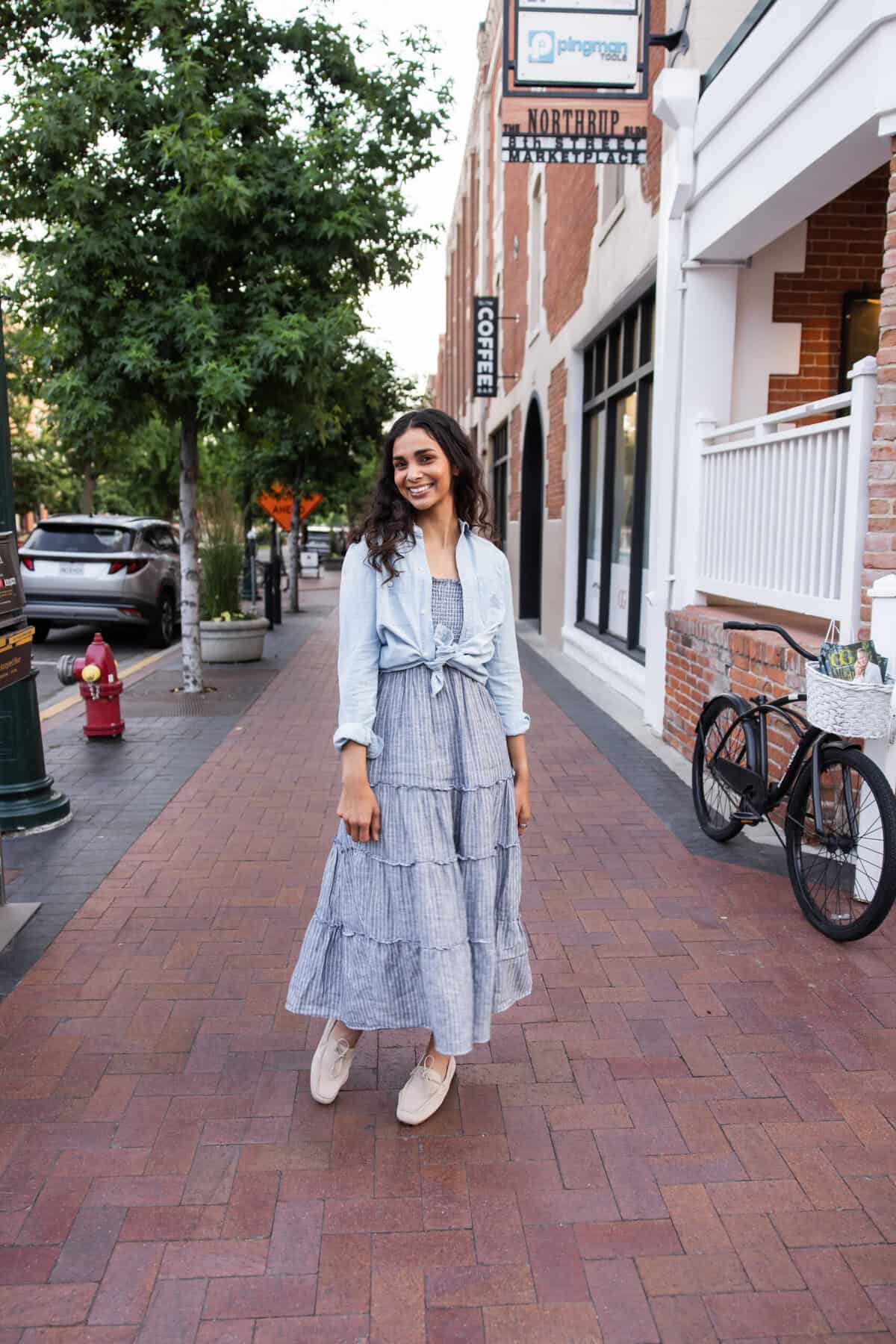 Nisha standing on cobblestone street wearing a long blue summer dress.