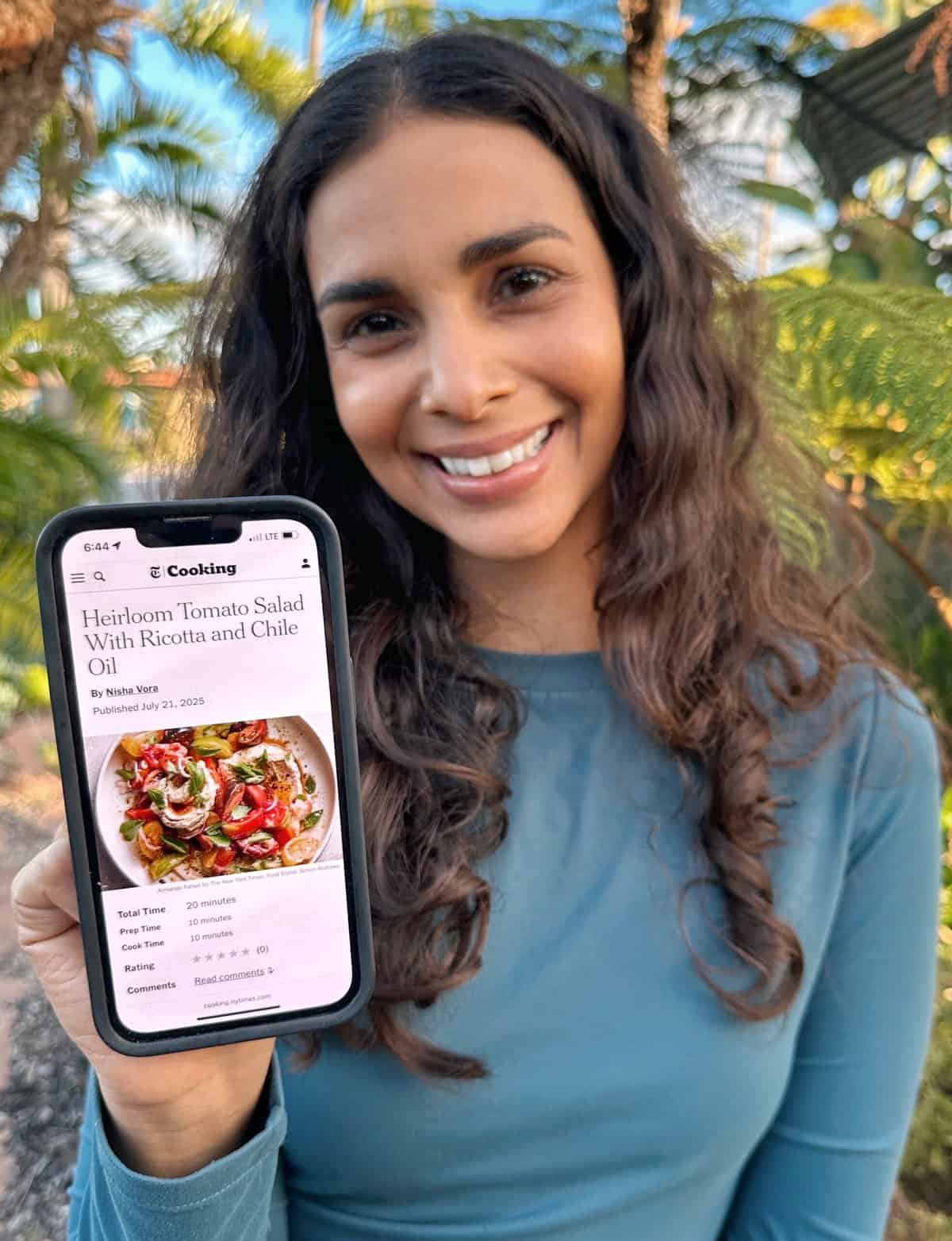 Nisha holding an iphone up with a recipe on the screen. 