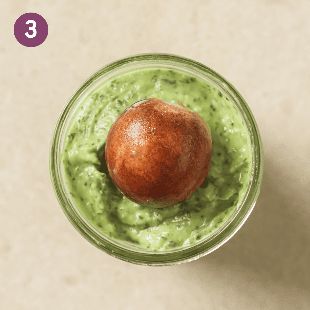 avocado pit on top of avocado crema in a glass bowl.
